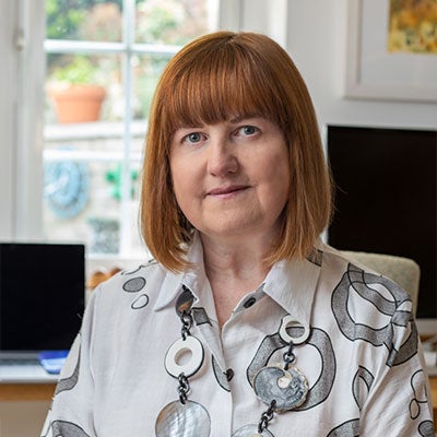 A photo of Kate Nash smiling. She has medium length brown hair and wears a white patterned shirt.