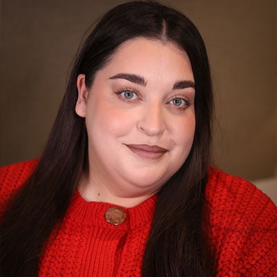 A photo of Danielle Vanier smiling. She has long, dark hair and wears a red cardigan. 