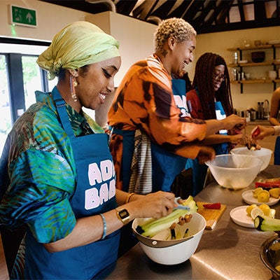 Three women wearing ADHD Babes aprons cooking in a kitchen