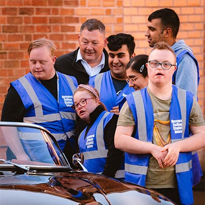 A group of disabled Evtec trainees stand in front of a car.