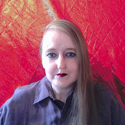 A photo of Jennie Kermode. She is wearing red lipstick and a purple shirt. Her long hair is parted to the side. 