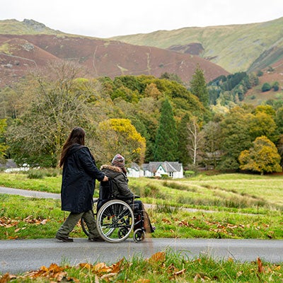 A woman pushing a person's wheelchair in the Lake District.