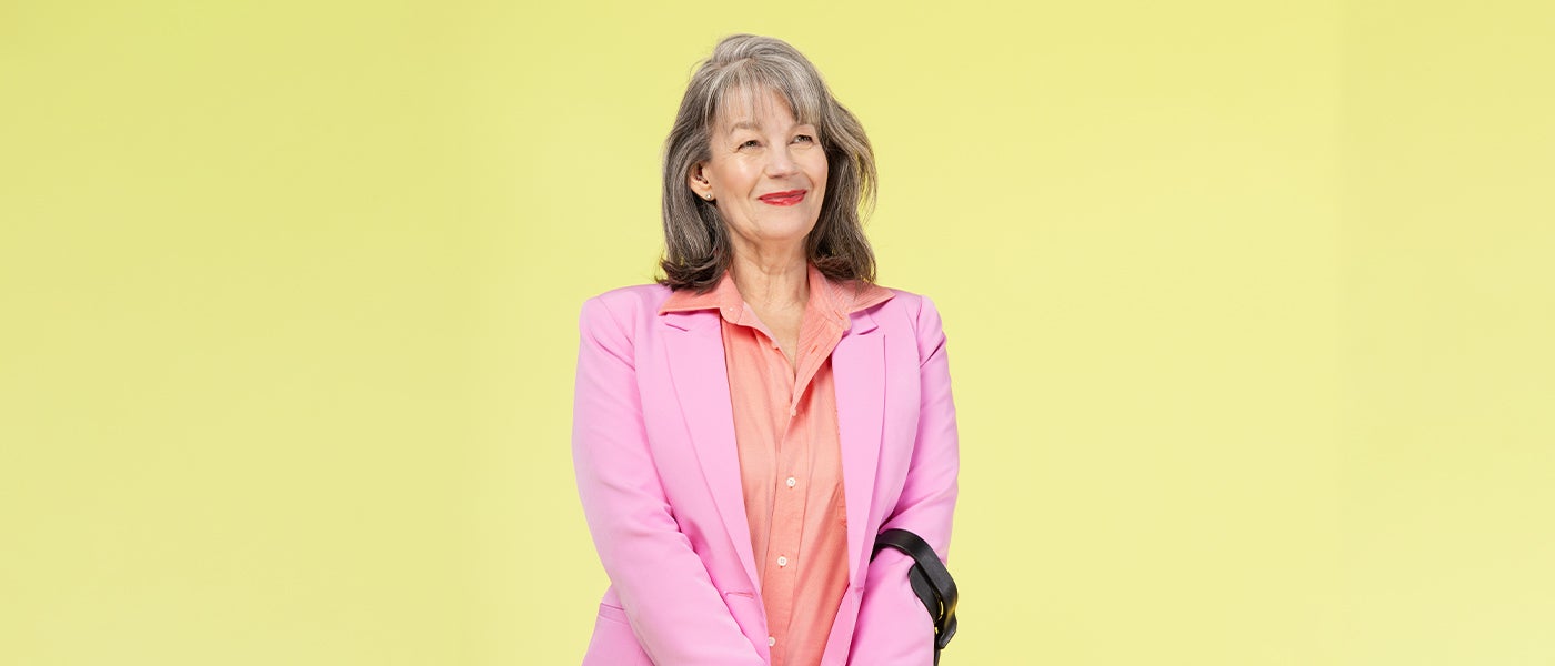 A woman with grey hair in a pink suit and orange shirt